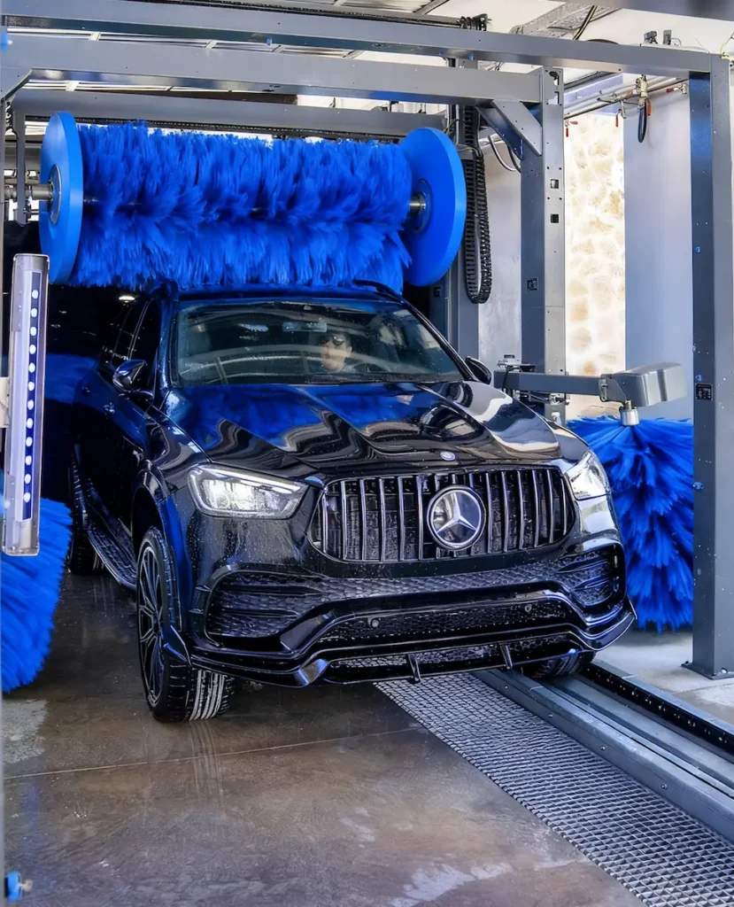 Een zwarte auto wordt gewassen in een wasstraat met grote blauwe borstels.